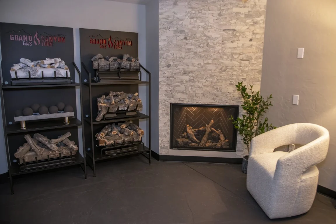 gas log display racks with six styles next to a gas fireplace with a white stone wall and a comfy chair